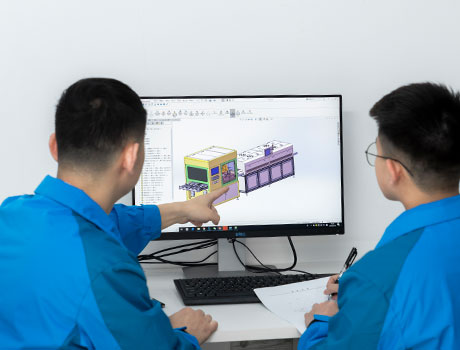 2 research personnel discussing in front of a computer showing engineering drawing of a machine layout
